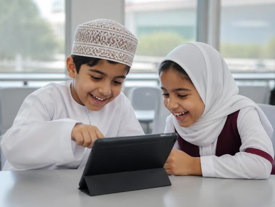 Two Omani children laughing while playing an English word game on a tablet