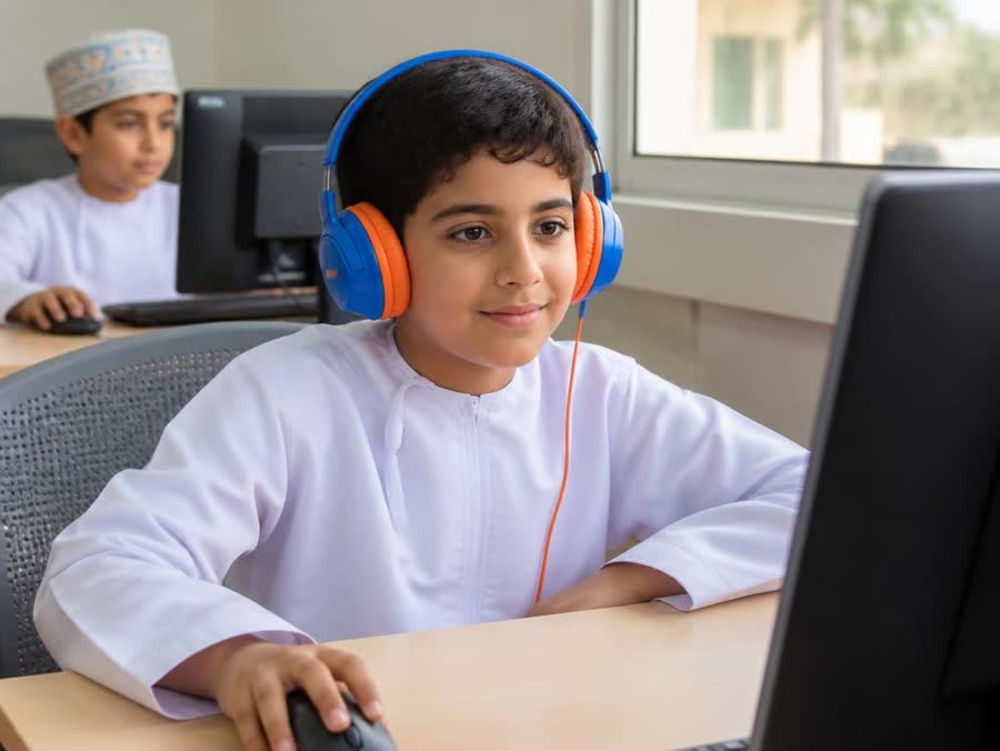 An Omani boy wearing headphones listening to English at a school computer